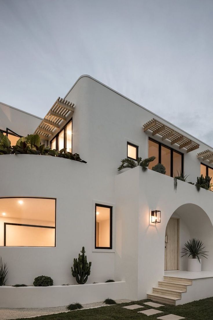 a white house with lots of windows and plants on the side of it at dusk