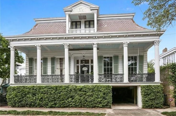 an old style house with white trim and columns on the front porch, surrounded by greenery