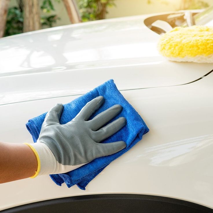 a person wearing gloves and holding a blue cloth on top of a white car