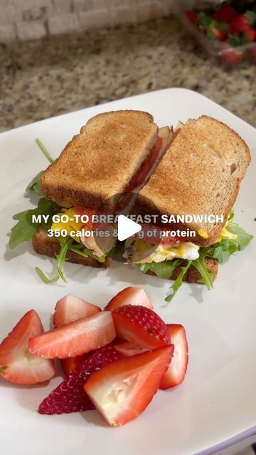 a white plate topped with a cut in half sandwich and strawberries