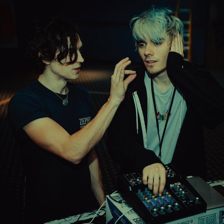 two young men standing next to each other in front of a dj's mixer