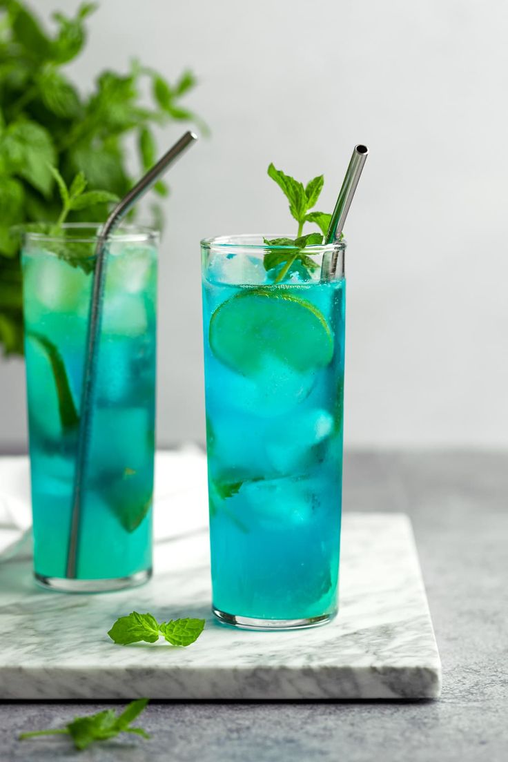 two glasses filled with blue liquid and mint garnish on a marble counter top