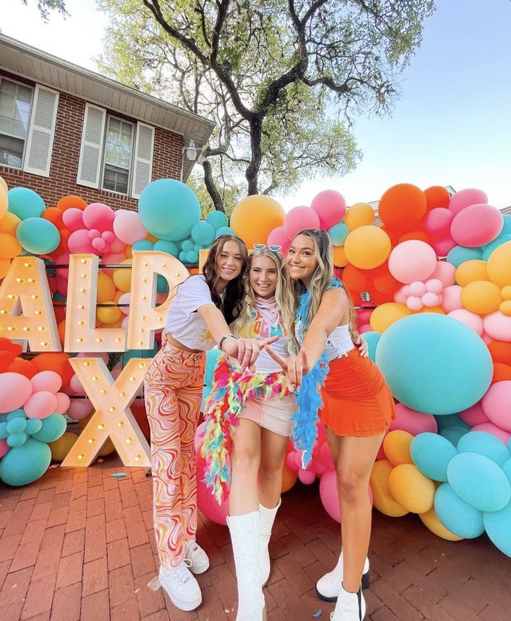 three girls standing in front of a balloon wall