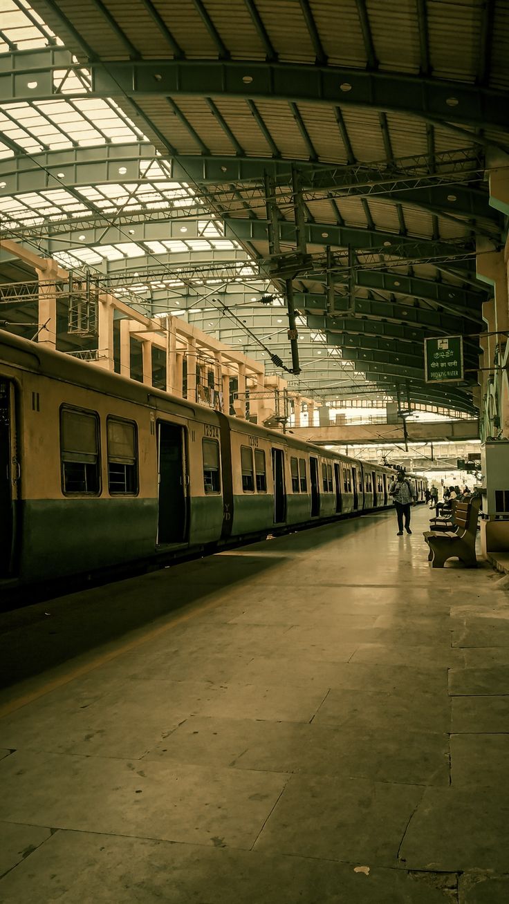 an empty train station with two trains parked next to each other and people walking on the platform