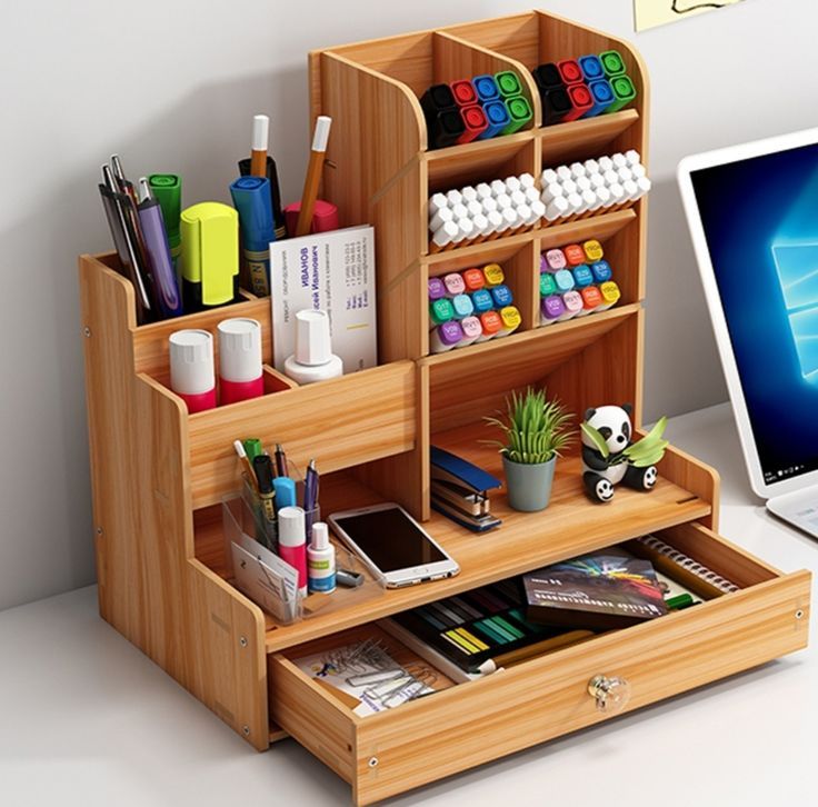 an open laptop computer sitting on top of a desk next to a wooden shelf filled with office supplies