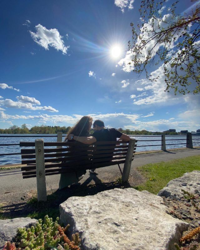 two people are sitting on a bench by the water with their backs to each other