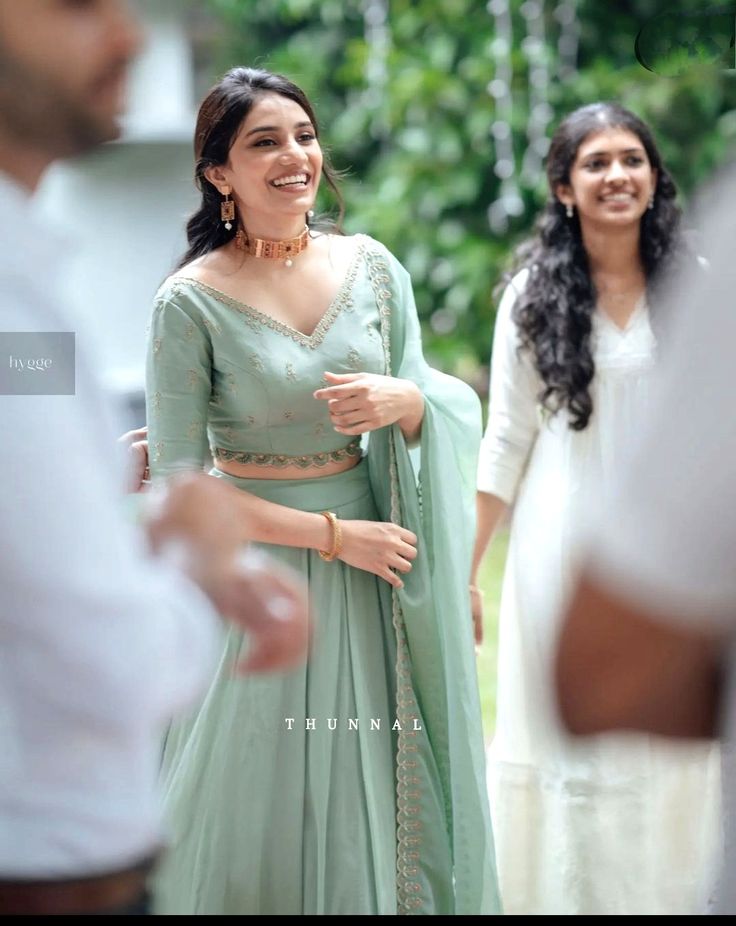 a woman in a green lehenga smiles as she stands next to other people