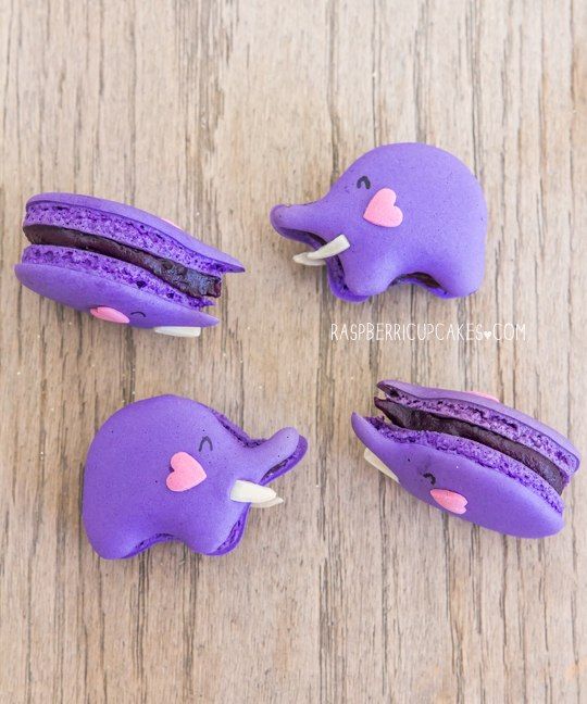 purple elephant cupcakes with pink hearts on them sitting on a wooden table next to each other