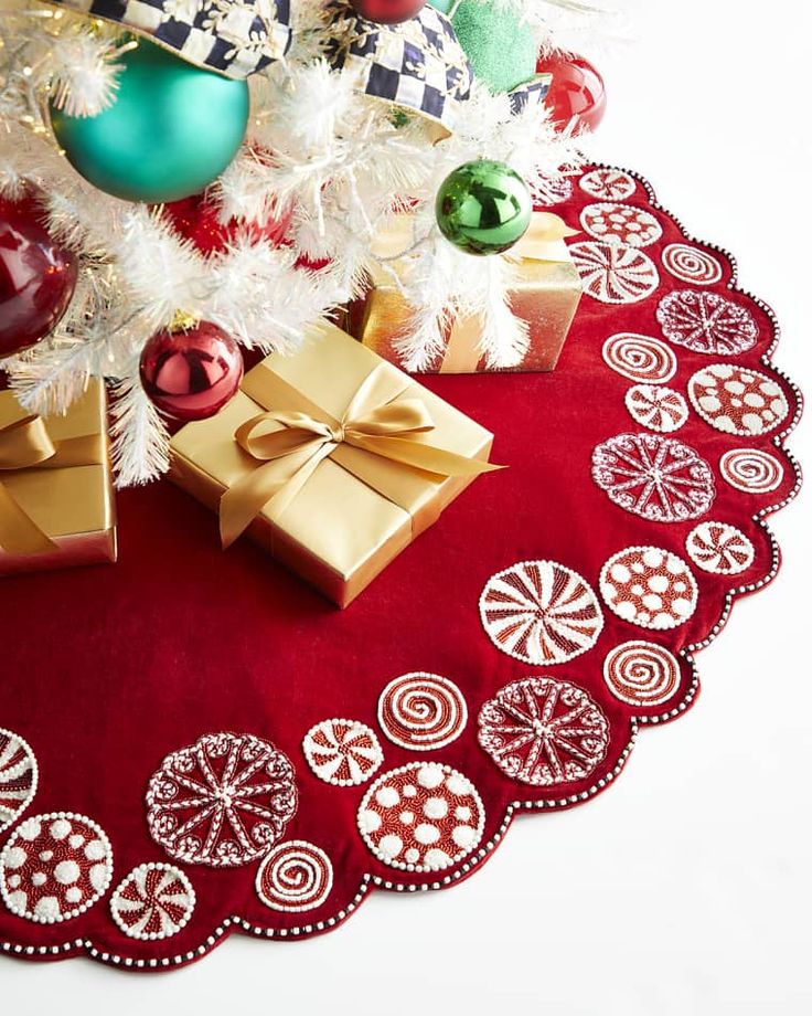 a christmas tree with ornaments and presents on the floor next to a red tablecloth