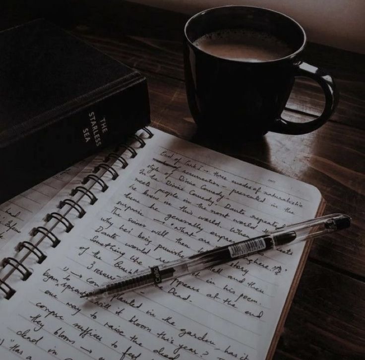 an open notebook with writing on it next to a cup of coffee and a pen