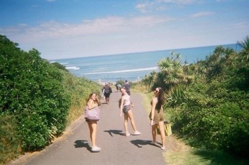 three girls walking down the road near the ocean with their backs turned to the camera