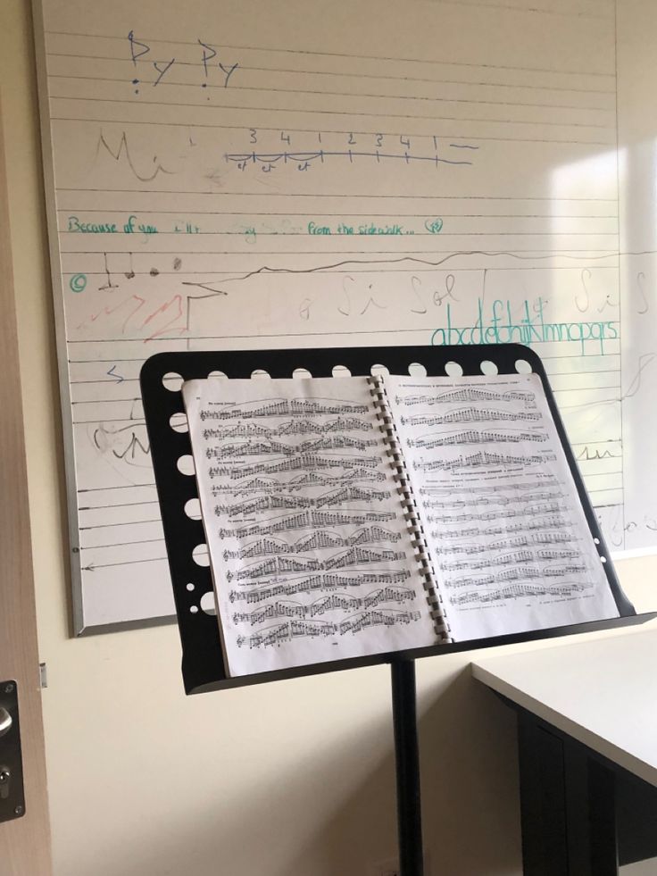 an open note book sitting on top of a black stand next to a whiteboard