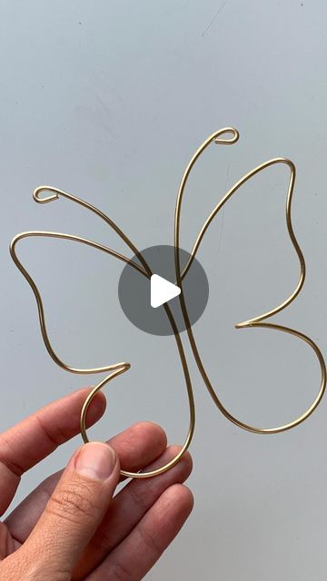 a hand holding a wire sculpture with a butterfly on it's back and an arrow in the middle