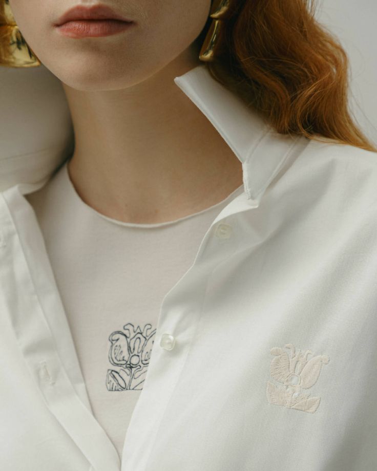 a woman with red hair wearing large gold hoop earrings and a white button up shirt