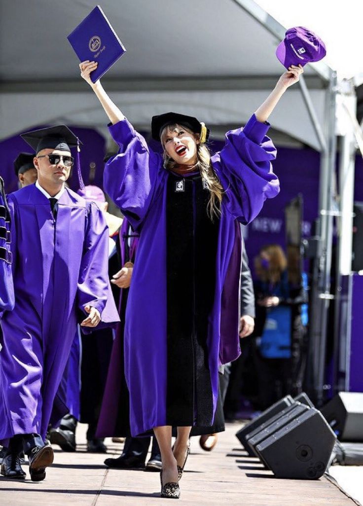 a woman in purple graduation gown and hat holding up her diploma while other people walk by