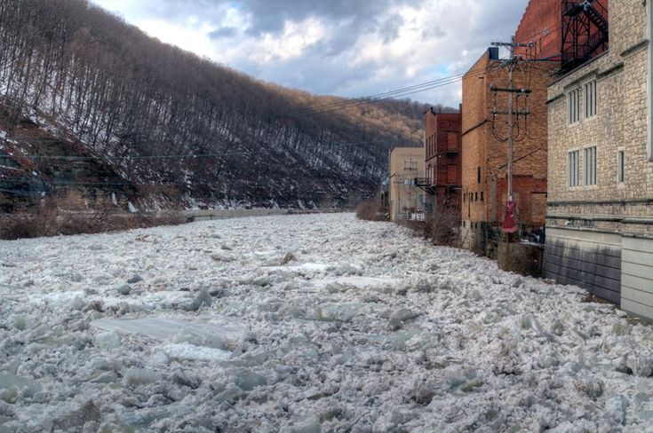 there is snow on the ground and water in the river next to some buildings with mountains in the background