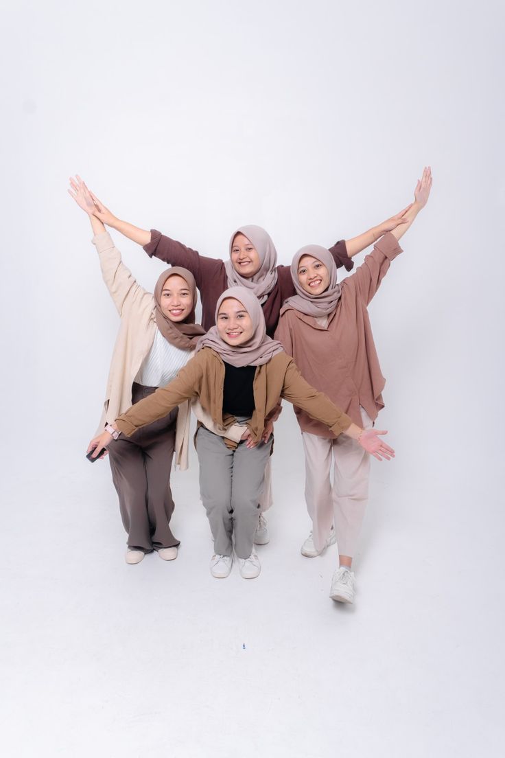 four women in hijabs are posing for the camera with their arms spread out