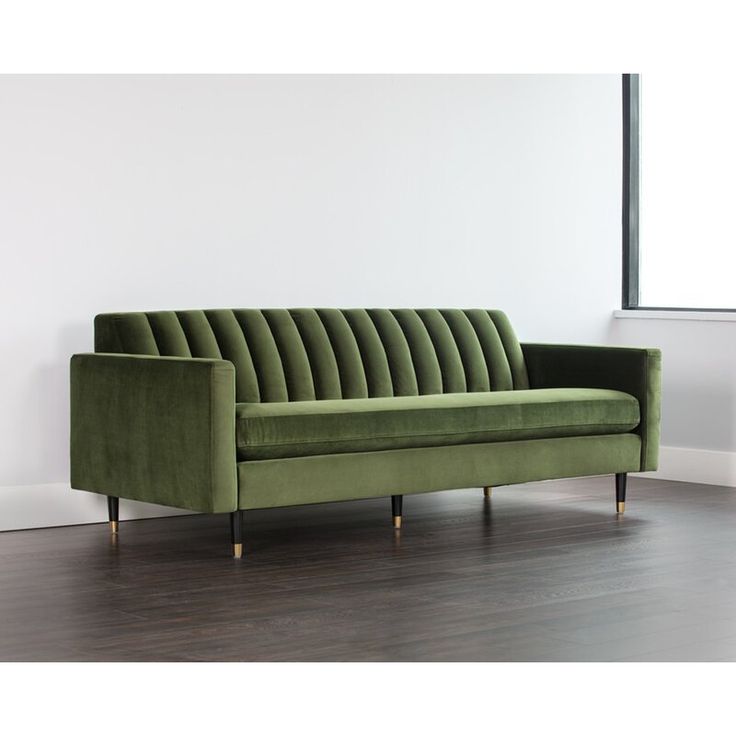 a green velvet couch sitting on top of a hard wood floor next to a window