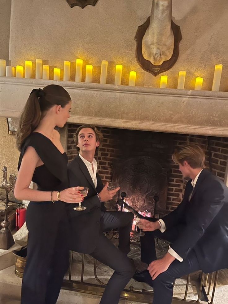 two men and a woman standing in front of a fire place with candles on it