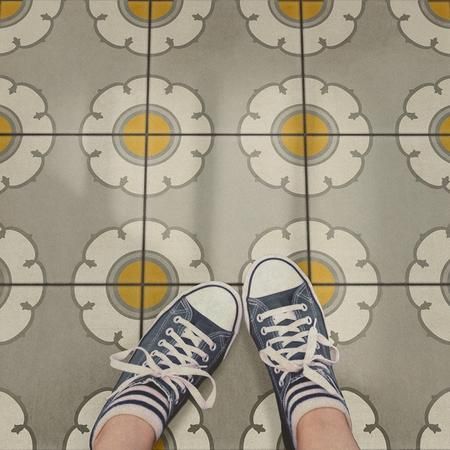 a person standing on a tiled floor with their legs crossed and shoes in the air