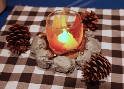 a lit candle sitting on top of a checkered table cloth with pine cones around it