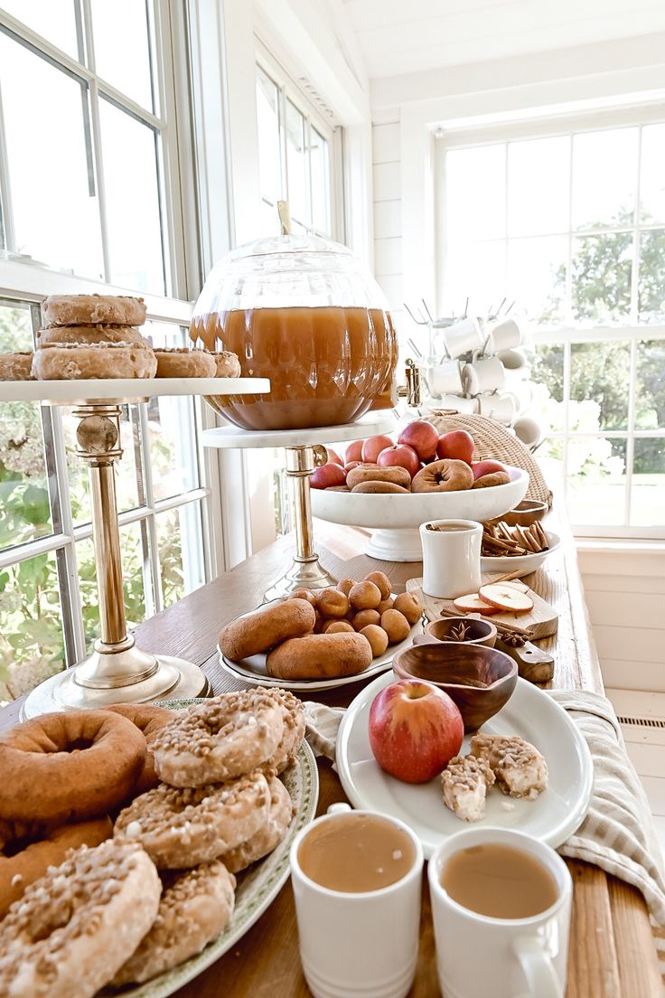 an assortment of donuts, apples, and coffee on a table in front of a window