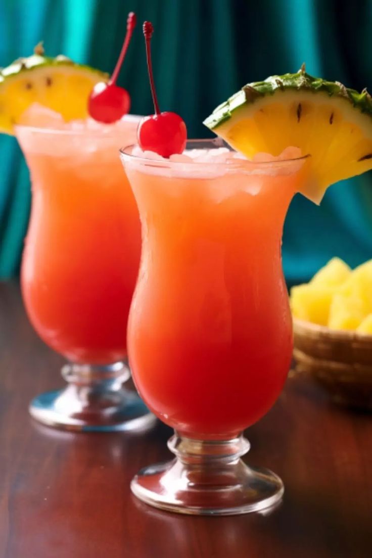 two glasses filled with drinks sitting on top of a table next to pineapples