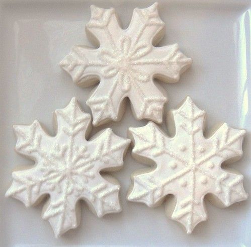 three white frosted cookies with snowflakes on them are sitting on a plate