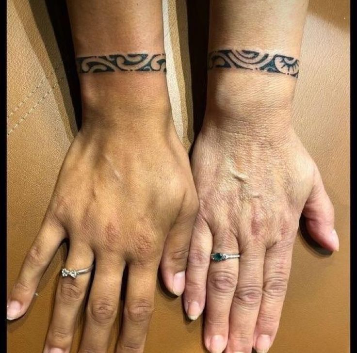 two people with matching tattoos on their arms and wristbands, both holding each other's hands