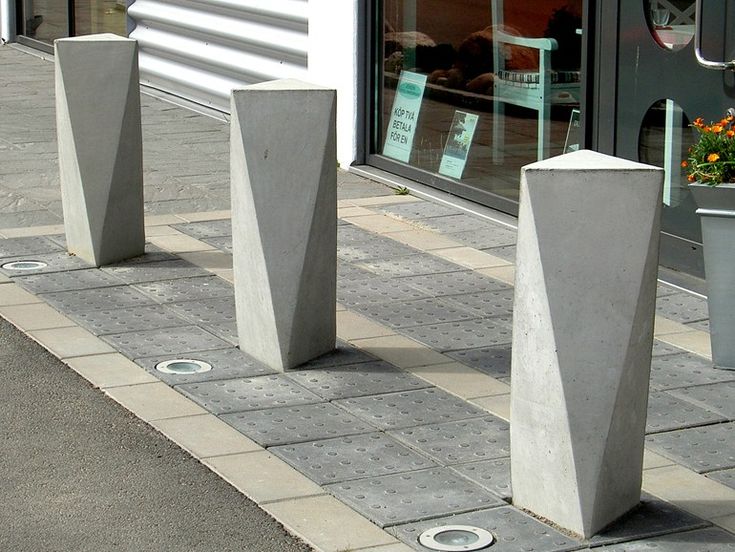 three cement vases sitting on the side of a road next to a sidewalk with potted plants in front of it