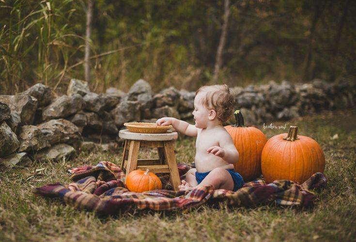 a baby sitting in the grass with pumpkins