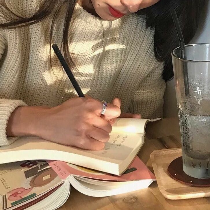 a woman sitting at a table writing on a book with a glass of water in front of her