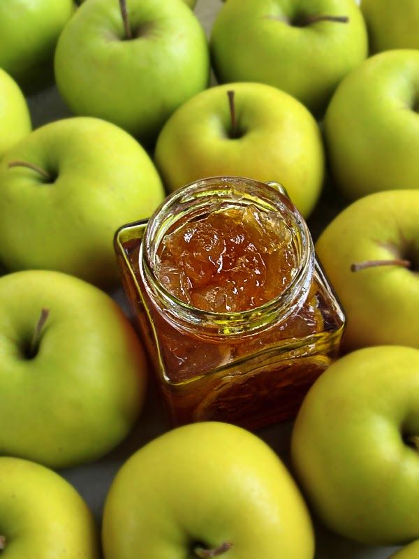 there are many green apples with jam in the jar on top and one is yellow