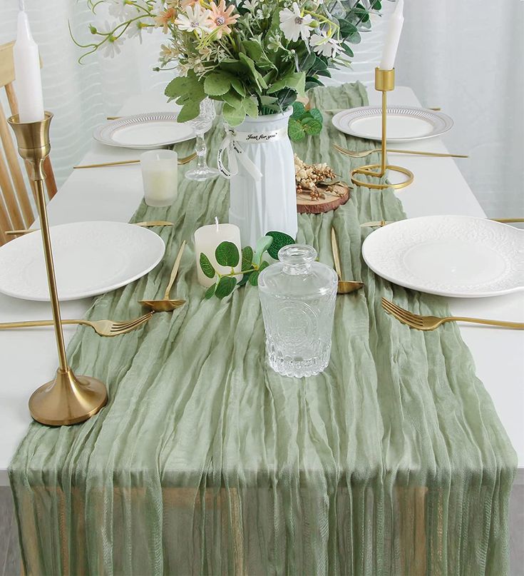 the table is set with white plates and green cloths, gold candlesticks and flowers