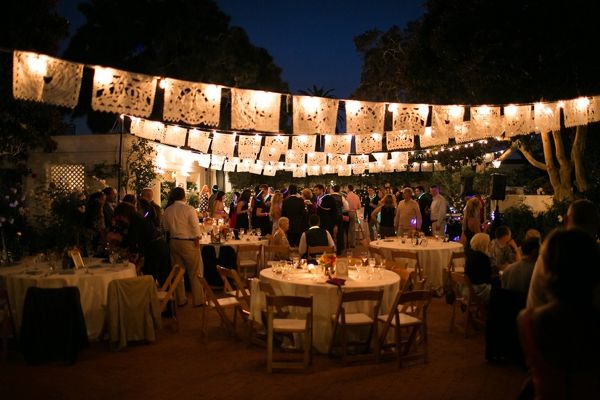 a group of people standing around tables with lights strung over them and hanging from the ceiling