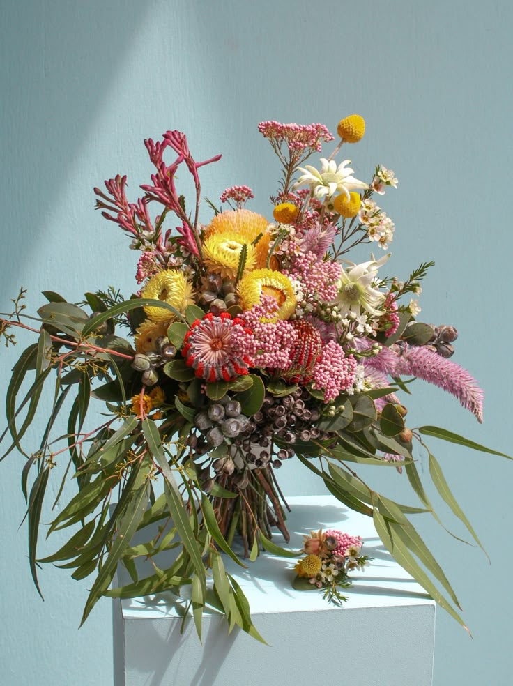 a vase filled with lots of colorful flowers on top of a white table next to a blue wall