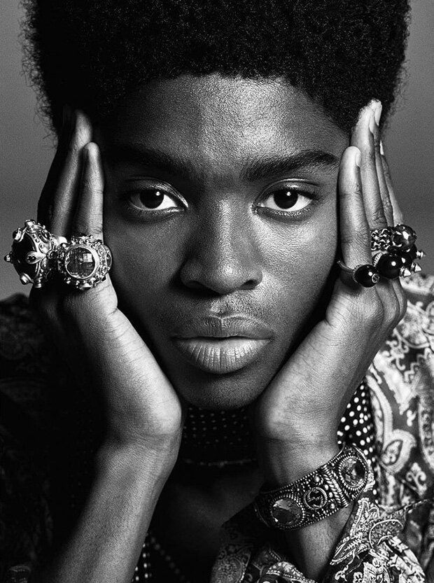 a black and white photo of a man with rings on his hands, looking at the camera