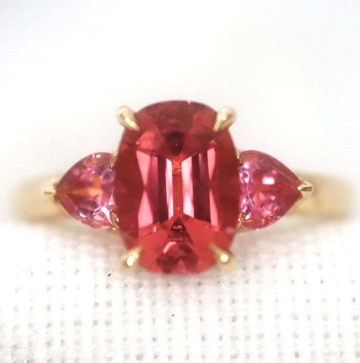 Introducing a stunning piece of jewelry that will brighten up any outfit - an orange pink tourmaline ring set in 14K yellow gold. Crafted with care and attention to detail, this ring showcases a beautiful oval-shaped orange pink tourmaline at its center. The gemstone is expertly faceted to catch the light and showcase its stunning natural color variations, ranging from deep orange to bright pink. Surrounding the gemstone is a 14K yellow gold setting, which adds a warm, luxurious touch to the pie Tourmaline Ruby Ring With Accent Stones For Promise, Pink Tourmaline Sapphire Ring As Birthstone, Red Tourmaline Gemstone Ring, Pink Tourmaline Gemstone Rings, Pink Tourmaline Birthstone Ring, Pink Tourmaline Rings, Pink Tourmaline Rings With Gemstone Accents, Fine Jewelry Red Tourmaline Rings, Red Tourmaline Rings Fine Jewelry