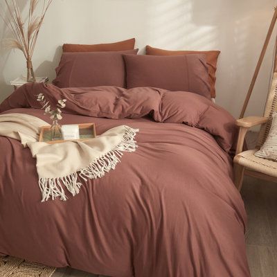 a bed with brown sheets and pillows in a room next to a wooden rocking chair