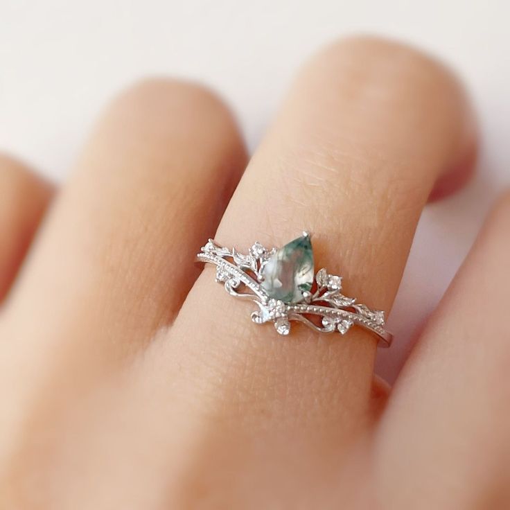 a close up of a person's hand with a ring on their finger that has a green stone in the middle