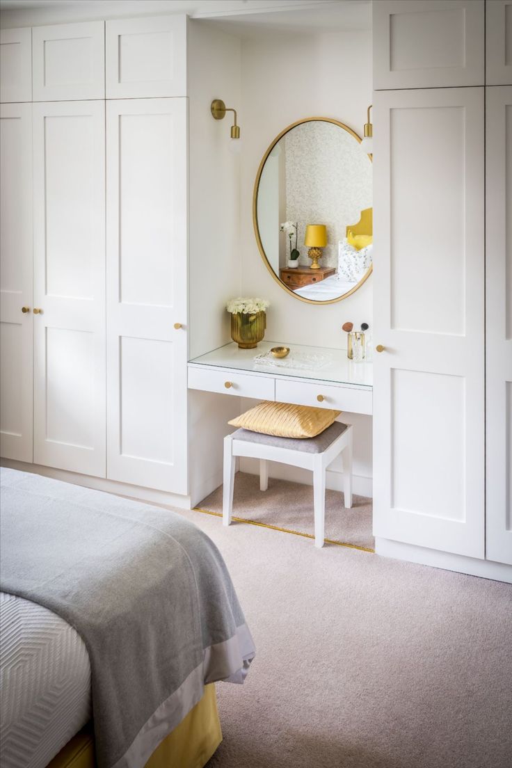 a bedroom with white cabinets and a mirror on the wall over a small table next to a bed