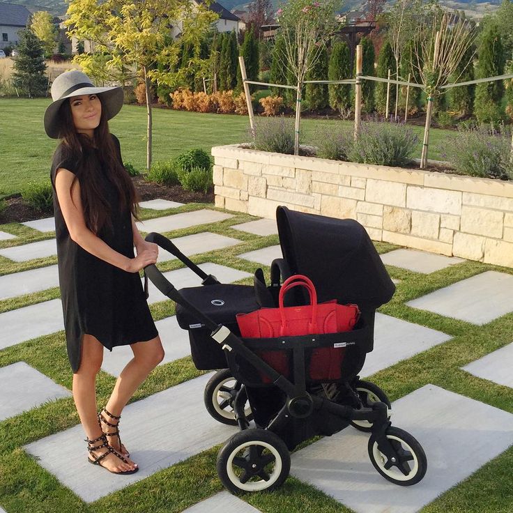 a woman standing next to a stroller with a red bag on the front and side