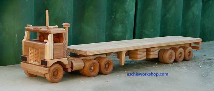 a wooden toy truck with a trailer attached to it's flatbed parked in front of a green wall