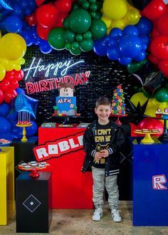 a young boy standing in front of a birthday cake and balloon arch at a party