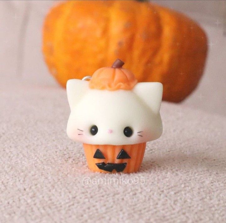 a small white cat figurine sitting on top of a table next to a pumpkin