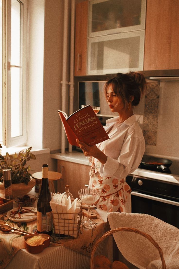 a woman standing in a kitchen reading a book