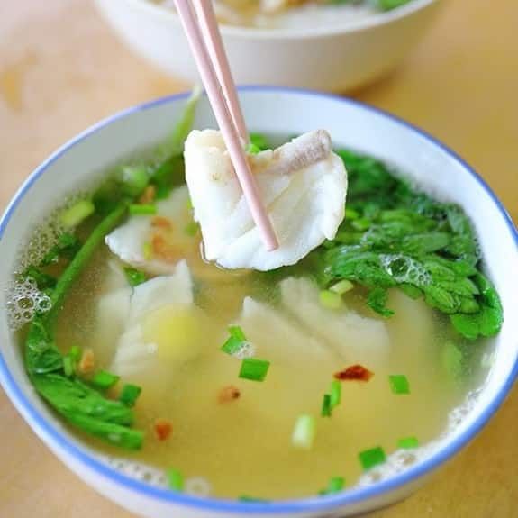 a person holding chopsticks above a bowl of soup