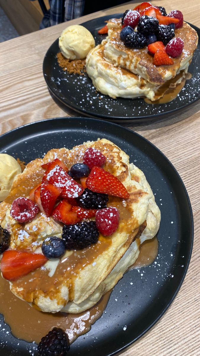 two black plates topped with pancakes covered in fruit