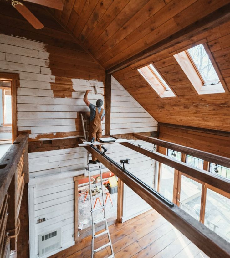 a man standing on top of a ladder in a room filled with wooden walls and windows