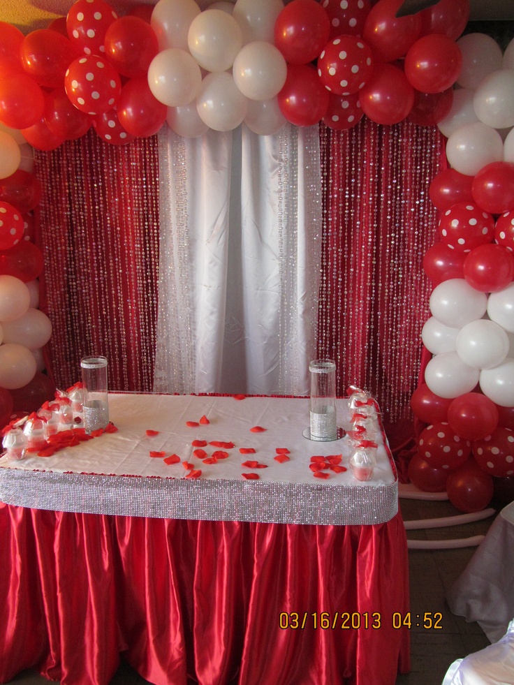 a table with red and white balloons on it next to a stage set up for a party